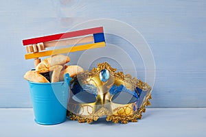 Purim celebration concept with hamantashen cookies, Purim mask and toy noisemaker on blue background