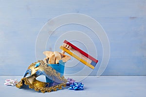 Purim celebration concept with hamantashen cookies, Purim mask and toy noisemaker on blue background