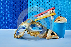 Purim celebration concept with hamantashen cookies, Purim mask and toy noisemaker on blue background