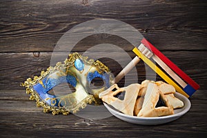 Purim celebration concept with hamantashen cookies, Purim mask and toy noisemaker on wooden background