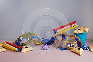 Purim celebration concept. Hamantashen or haman ears, noisemaker and mask on grey background