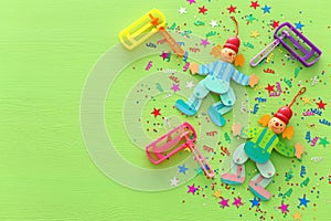 Purim celebration concept & x28;jewish carnival holiday& x29;, clowns, confetti and noisemaker over wooden green background.