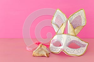 Purim celebration concept jewish carnival holiday with cute rabbit mask, noisemaker and hamantash cookies over wooden table