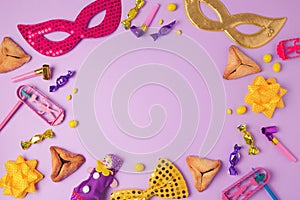 Purim holiday concept with carnival mask, hamans ears cookies and party supplies on purple background.