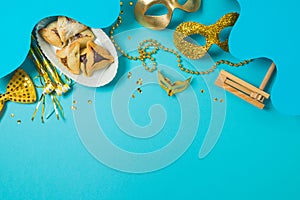 Purim holiday concept with carnival mask, noisemaker and hamantaschen cookies on blue background.