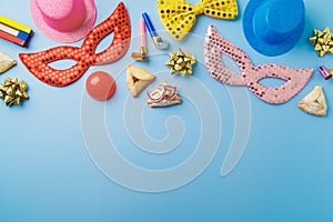 Purim holiday concept with carnival mask, noisemaker, hamantaschen cookies and party supplies on blue background. Top view, flat