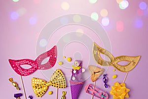 Purim holiday concept with carnival mask and party supplies on purple background with bokeh lights.