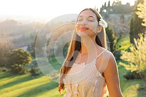 Purity and beauty concept. Portrait of beautiful girl breathing fresh air outdoor in nature with white dress and flower on ear