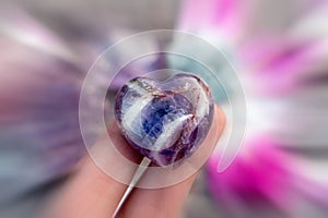 Purple amethyst crystal heart in a female hand, crystals in the bg, radial blur