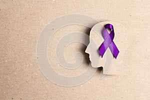 Purple awareness ribbon and head silhouette on a brown cardboard background. E