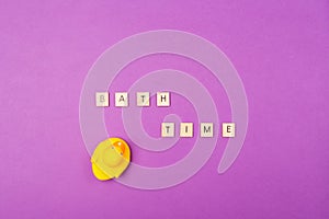 Purple background with wooden letters Bath Time and rubber yellow duck. Top view. Flat lay. Bath child theme concept.