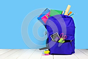 Purple backpack full of school supplies against a blue background. Back to school. photo