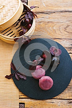 A Purple bamboo steamer filled with cherries is displayed on a wooden table.Mochi asian dessert