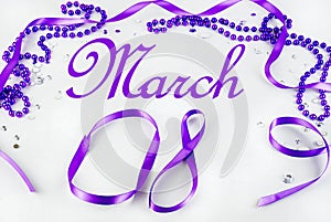 Purple beads and ribbon and sparkly jewels on a light background make a border for International Women`s Day on March 8th each