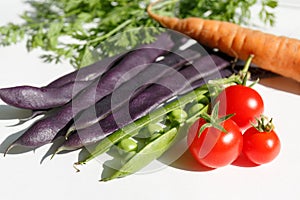 purple beans in pods, green peas in a pod, red cherry tomatoes, greens and raw carrots