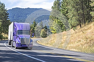 Purple big rig semi truck with reefer semi trailer running with load on the winding mountain road
