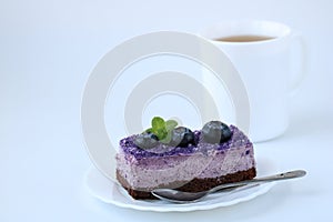 Purple blueberry mousse cake with blueberry on white plate with teaspoon and cup of tea on white background, horizontal