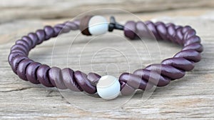 a purple bracelet with two white beads on a wooden surface with a black bead clasp and a brown leather cord with a white bea