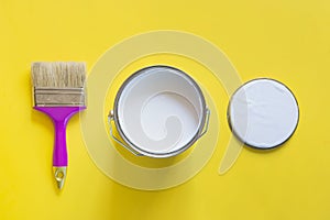 Purple brush with open can of white paint on yellow background. Trend concept