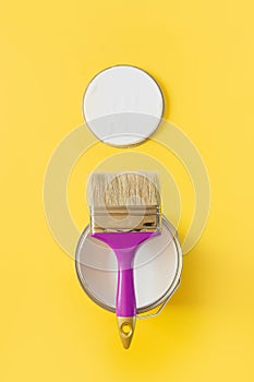 Purple brush with open can of white paint on yellow background. Trend repairs concept