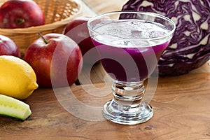 Purple cabbage juice in a glass, with cabbage and apples in the