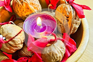 Purple candle with decorated wallnuts in a wooden bowl