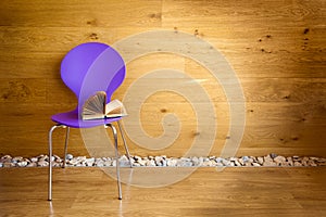 Purple chair with opened book next wooden wall