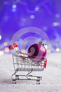 Purple Christmas ball in small supermarket trolley with garland