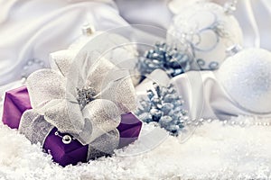 Purple Christmas package with a silver ribbon and background christmas decoration - Christmas balls pine cone white satin and whit