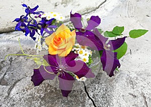 Purple clematis, delphinium, daisies on a stone background