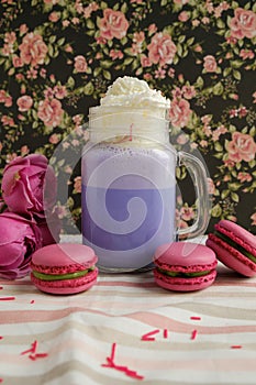 Purple coffee in stylized mason jar cup with macarons and roses and colorful decoration on background of floral pattern. Blueberry