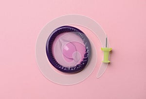 Purple condom and pin on pink background