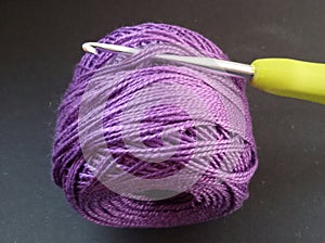 Purple crochet yarn and a crochet hook over black background.