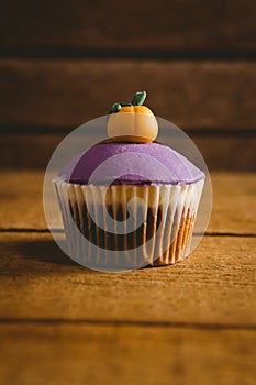 Purple cup cake with pumpkin icing on wooden table