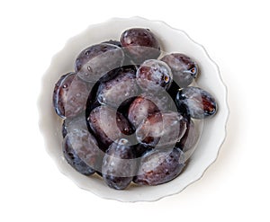 Purple damson plums in bowl top view isolated