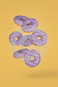 Purple decorated doughnuts with blueberries in motion falling or flying on yellow background