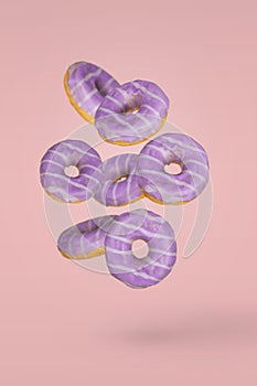 Purple decorated doughnuts in motion falling or flying on pink background