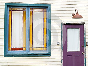 Purple door and green window in need of repaint in weatherboard