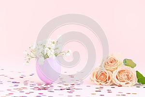 Purple easter eggshell with white gypsophila,yellow,orange pastel roses, pink background,multicolor confetti. Egg is symbol of