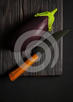 Purple eggplant with knife on wooden cutting board
