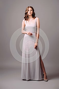 Purple evening dress with front slit. Luxury female gown. Young adult elegant lady in high heels, studio shot. Bridesmaids violet