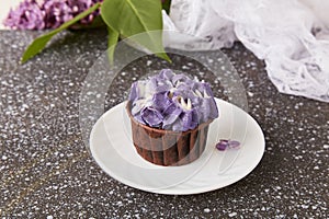 Purple floral cupcake among lilac flowers Spring background. French dessert