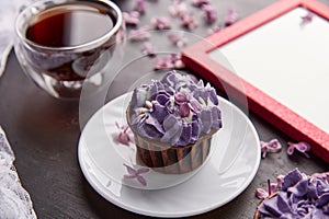 Purple floral cupcake using trendy Escapism trend. Frame mock up, cup of coffee among lilac flowers