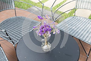 purple flower in glass vase, wicker chair on patio