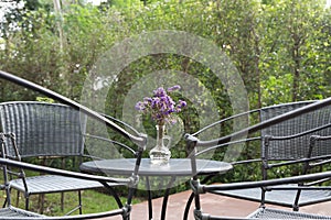 purple flower in glass vase, wicker chair on patio