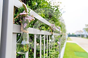A purple flowers in light bulb shaped vase hanging on home fence