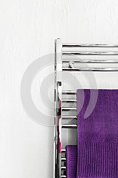 Purple fluffy terry towels hanging on stainless steel warmer rack installed in bathroom. White wall background. Interior design