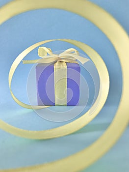 Purple Gift box at the end of the spiral yellow ribbon, blue background, vertical.