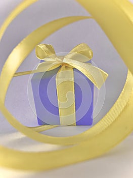 Purple Gift box at the end of the spiral yellow ribbon, grey background, vertical.