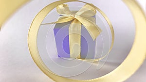 Purple gift box at the end of the spiral yellow ribbon, grey white background.